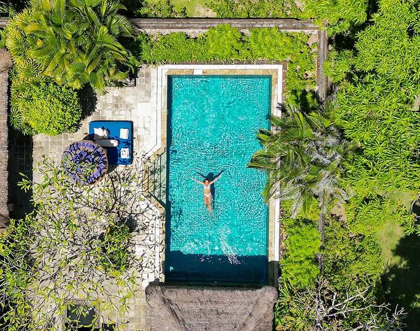 Woman swimming in resort pool surrounded by lush greenery The Oberoi Bali Woman swimming in resort pool surrounded by lush greenery The Oberoi Bali