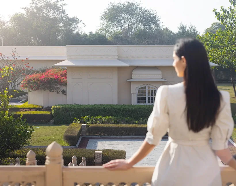 A woman overlooks The Oberoi Sukhvilas resort, surrounded by greenery. A woman overlooks The Oberoi Sukhvilas resort, surrounded by greenery.